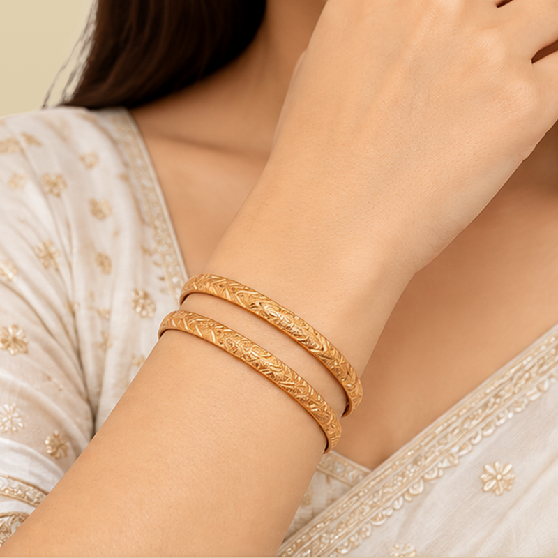 Golden floral vine bangles overlapping on a plain background