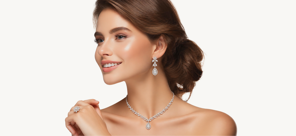 A woman with styled brown hair models a matching diamond necklace, drop earrings, and ring against a clean white background.